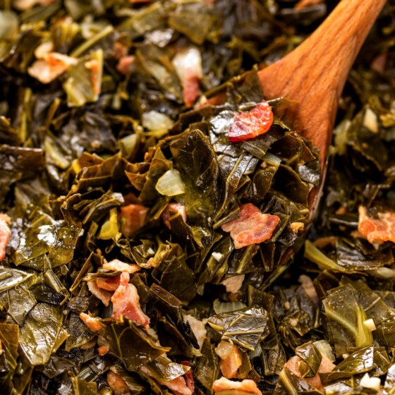 A serving spoon is dipping into a pot filled with cooked collard greens and bacon.