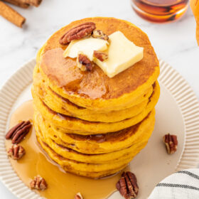 stack of pumpkin pancakes with maple syrup drizzled on top and garnished with whole pecans