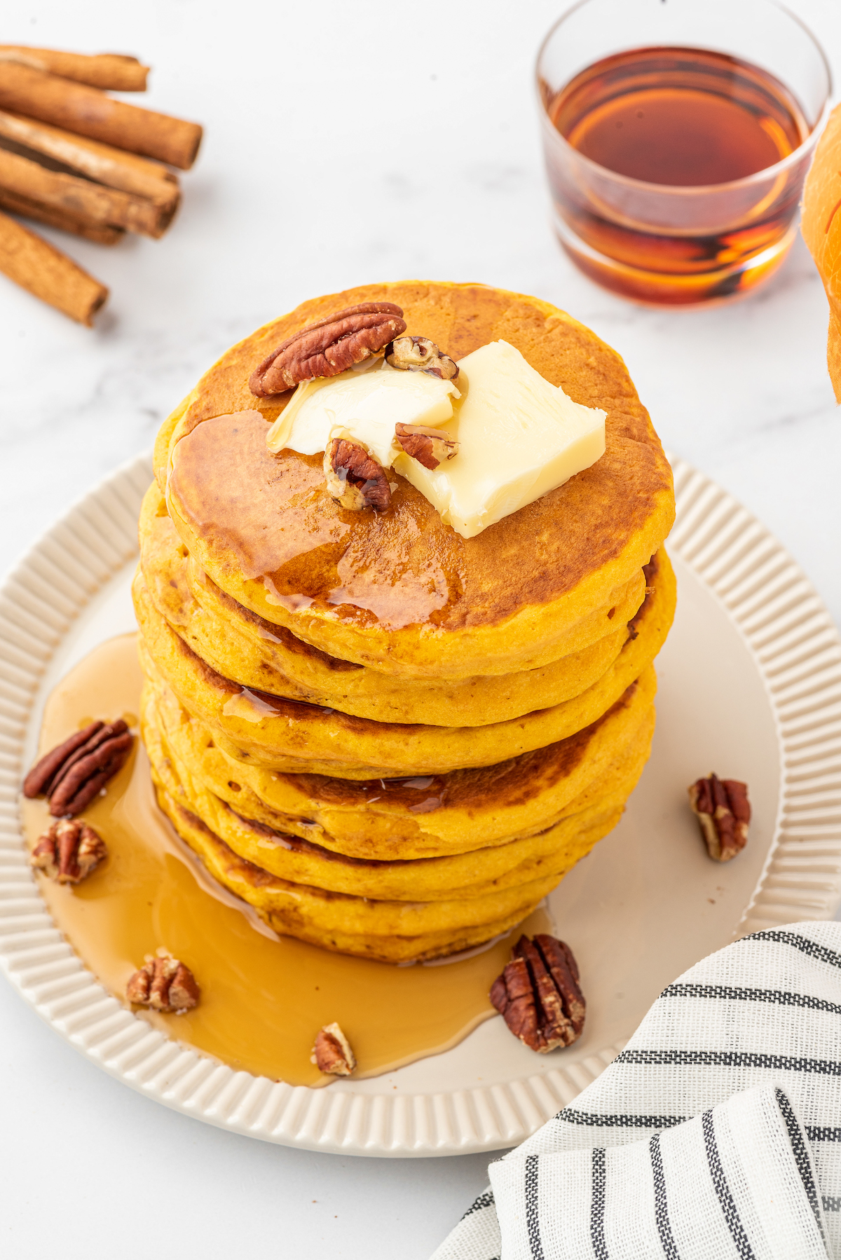 stack of pumpkin pancakes with maple syrup drizzled on top and garnished with whole pecans