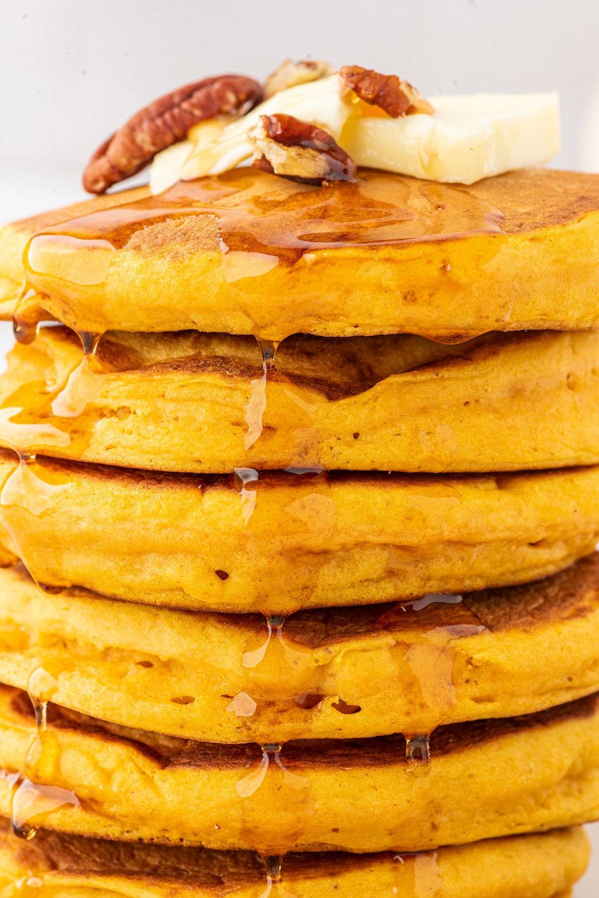 stack of pumpkin pancakes with maple syrup drizzled on top and garnished with whole pecans