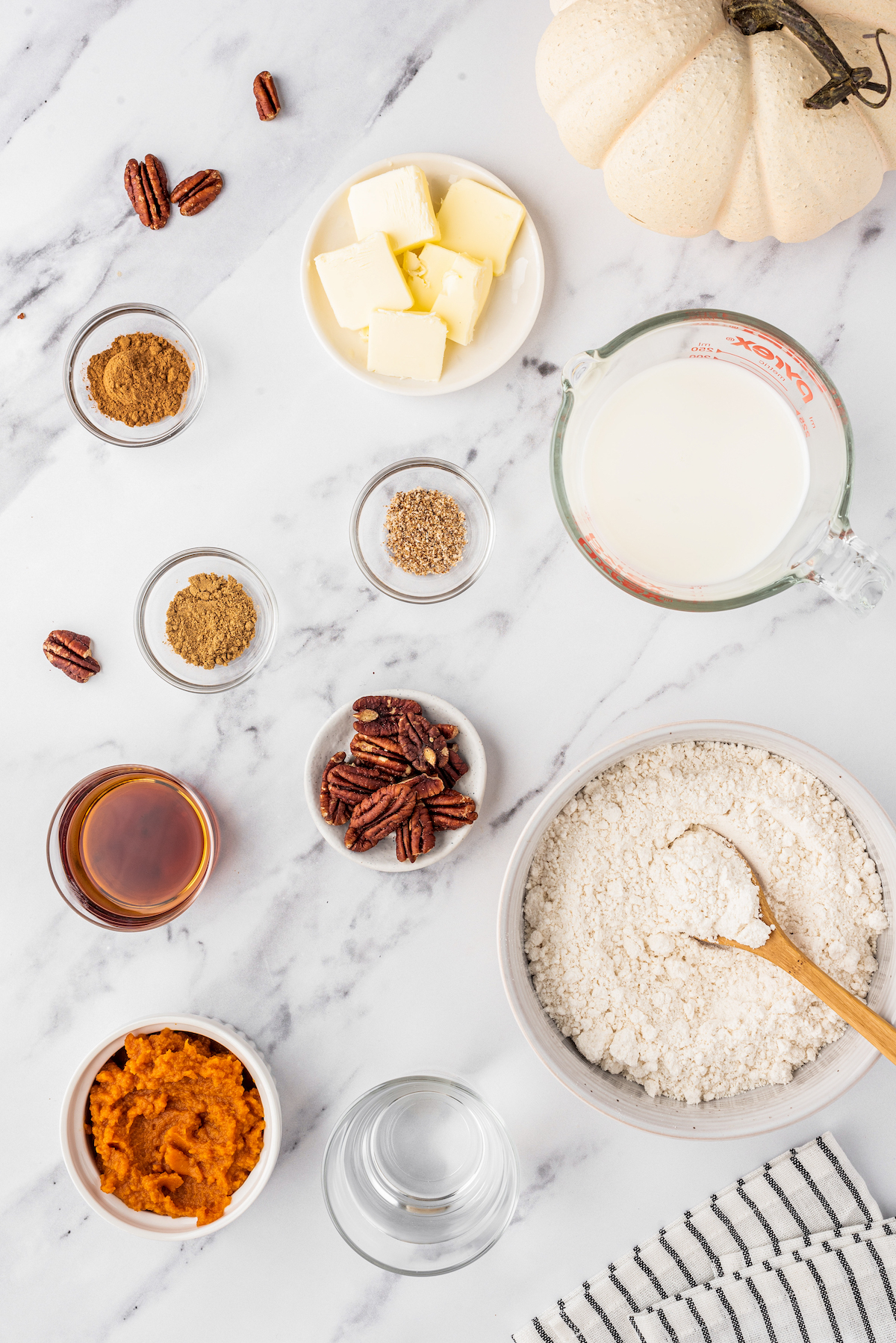 all of the ingredients to make pumpkin pancakes in individual bowls like pancake mix, milk, spices, pureed pumpkin, pecaons, and maple syrup