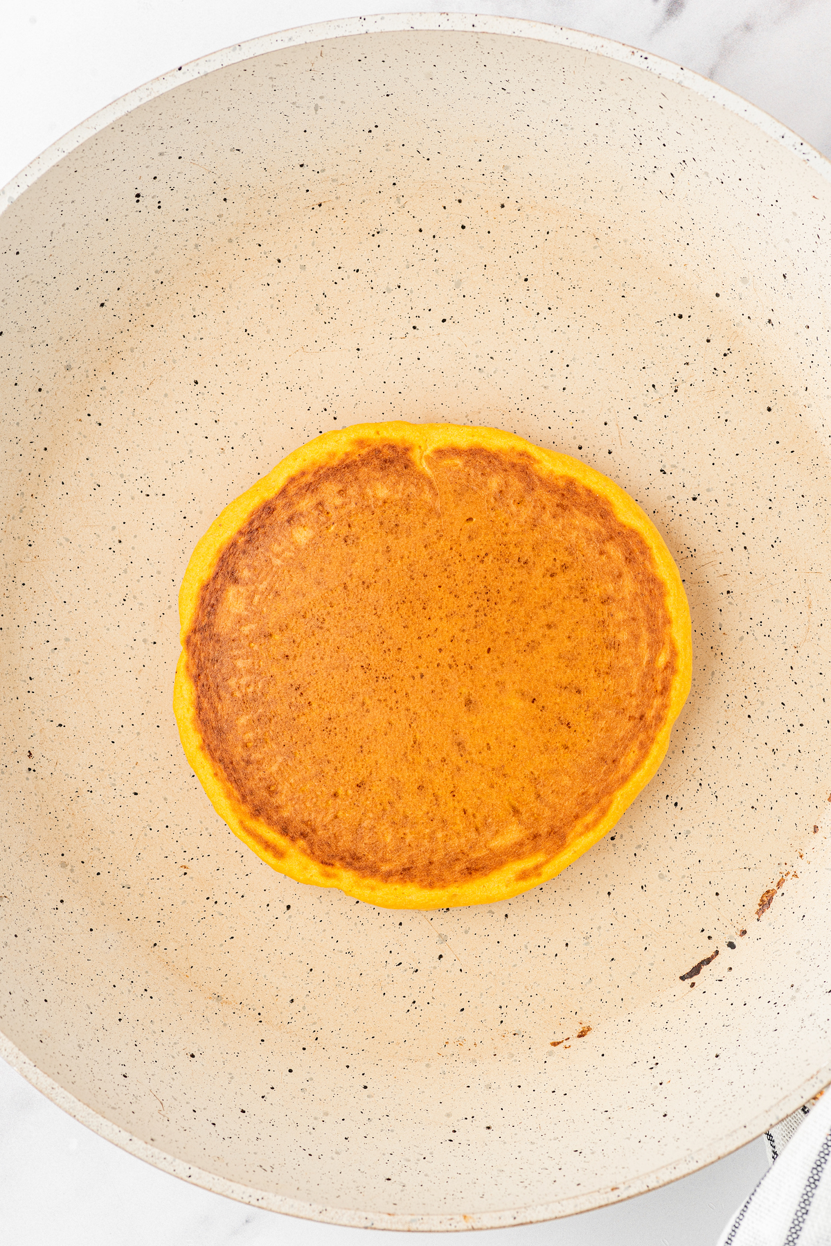 One pancake being cooked in a non-stick pan