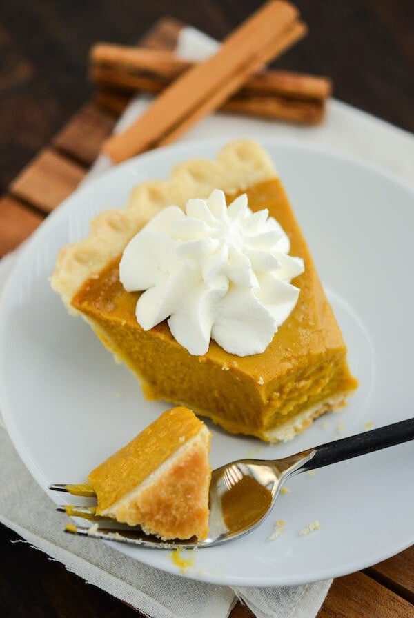 Buttermilk Pumpkin Pie topped with whipped cream on a white plate with a fork on a wooden board