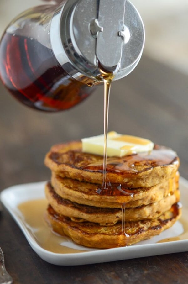 A stack of Pumpkin Pancakes on a white plate with syrup being poured over them
