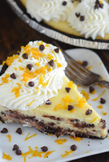 Cannoli Cheesecake on a white plate with a fork topped with whipped cream, orange zest, and chocolate chips