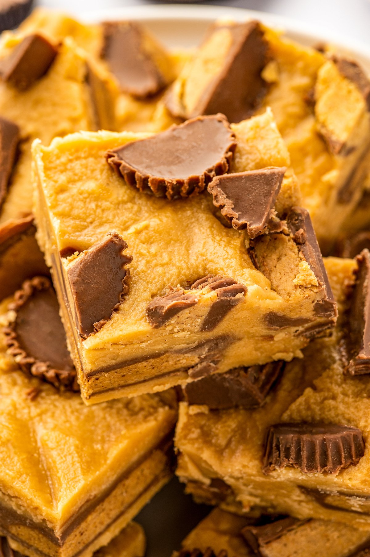 Close-up image of easy peanut butter fudge topped with peanut butter cups  that has been cut into squares and stacked on top of each other. 
