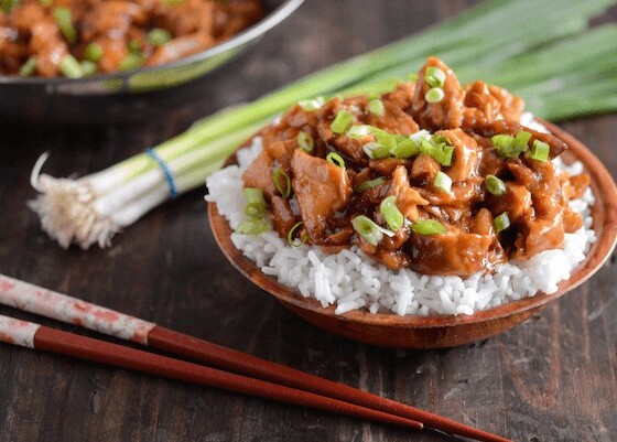 Crockpot Bourbon Chicken served over rice with chopsticks and scallions
