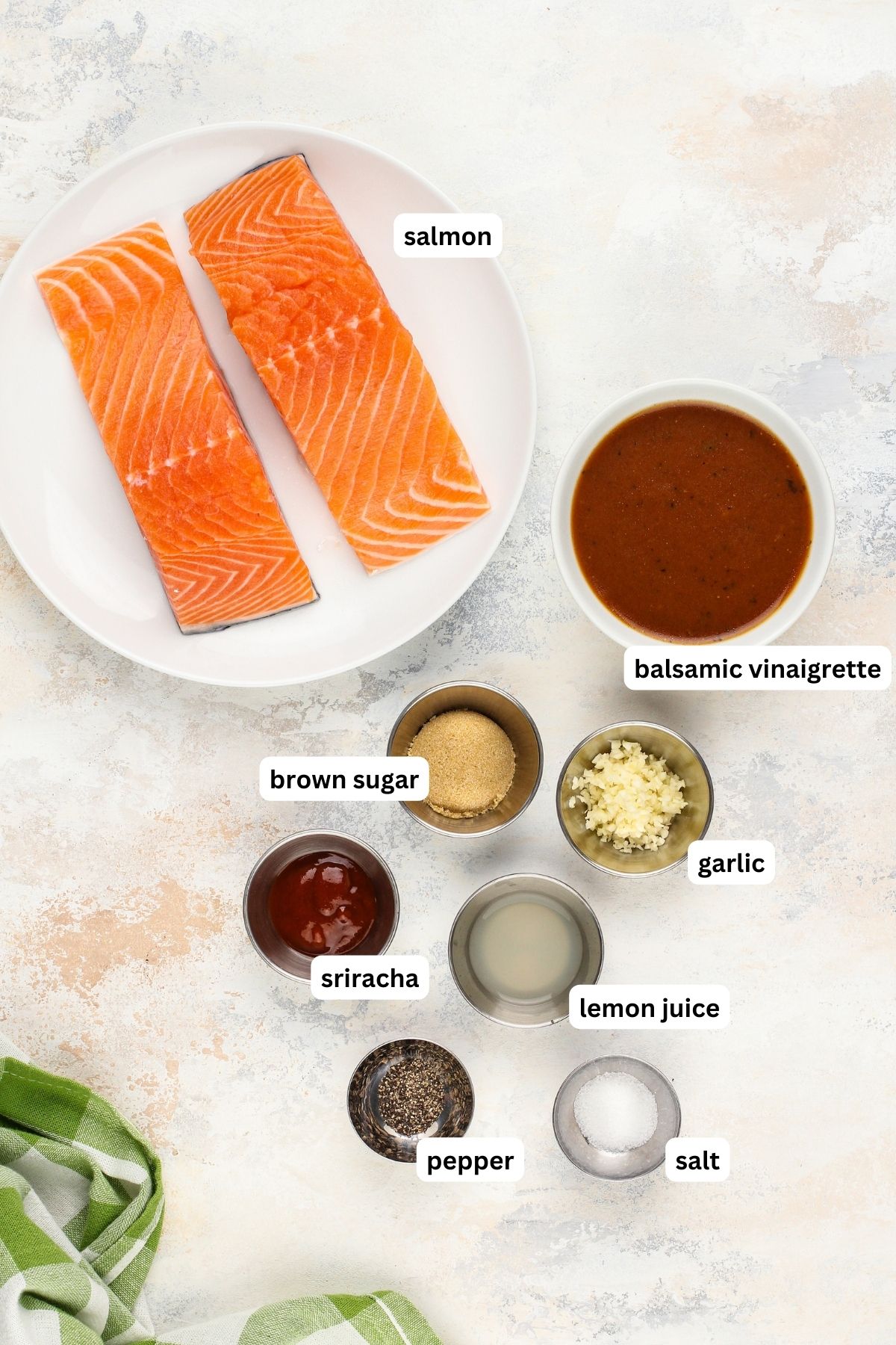 Labeled ingredients for balsamic salmon recipe arranged in bowls. From top to bottom: Salmon filets, balsamic vinaigrette, brown sugar, garlic, sriracha, lemon juice, pepper and salt.