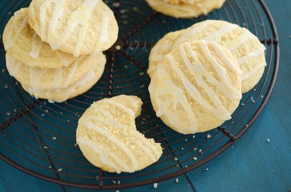 A Bunch of Lemon Chiffon Cookies on a Black, Circular Cooling Rack Over a Teal Tablecloth