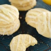 A Lemon Chiffon Cookie with a Bite Taken Out Beside More Iced Cookies on a Wire Rack
