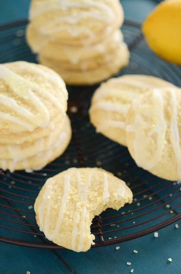 A Lemon Chiffon Cookie with a Bite Taken Out Beside More Iced Cookies on a Wire Rack