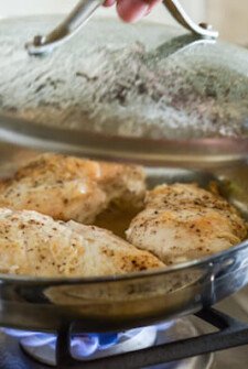 Chicken breasts being cooked in a covered skillet on a stove