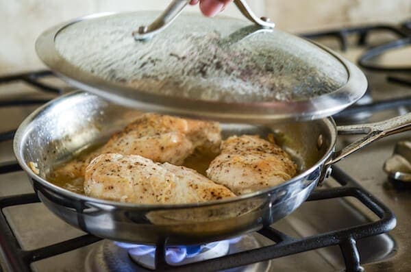 Chicken breasts being cooked in a covered skillet on a stove