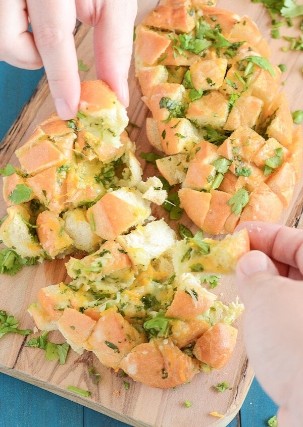 A loaf of bread filled with cheese and cilantro being pulled apart piece by piece