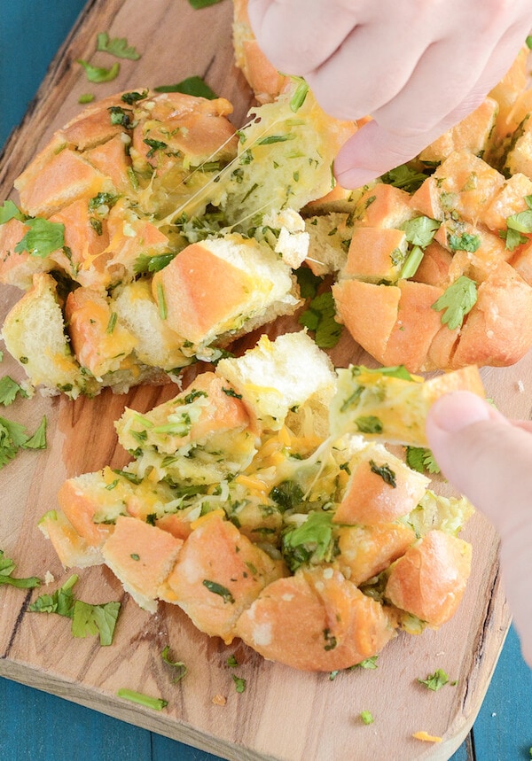 A loaf of cheesy bread with cilantro being pulled apart piece by piece
