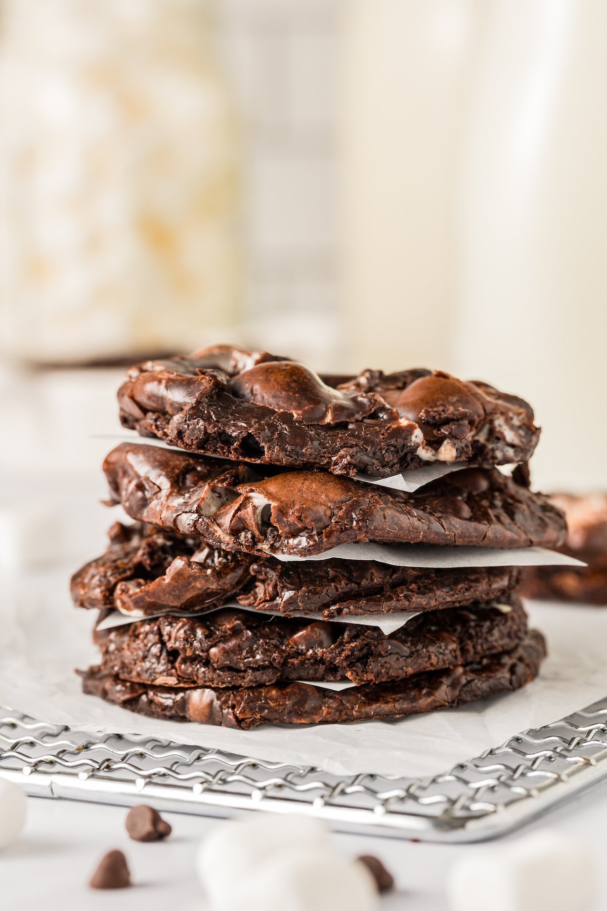 Chewy, crackly, and oh-so-gooey, these Marshmallow Chocolate Fudge Cookies are packed with chocolatey goodness and dangerously easy to make. Chocolate marshmallow cookies stacked on a rack, with squares of wax paper between each one.