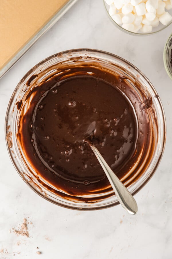 Stirring flourless chocolate cookie batter in a large, glass mixing bowl.