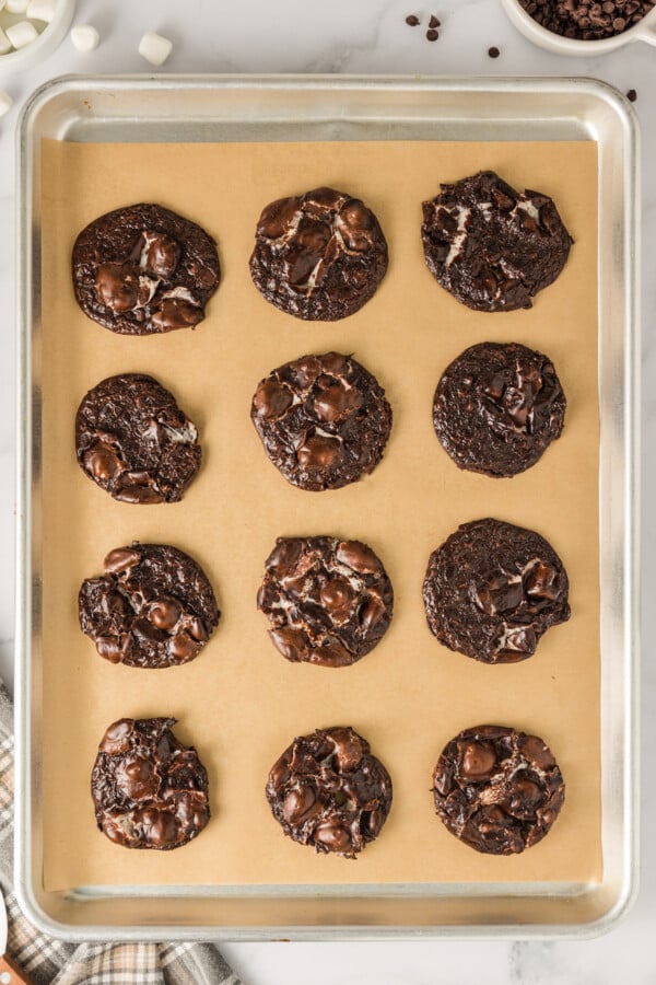 Baked chocolate marshmallow cookies on a parchment-lined baking sheet.