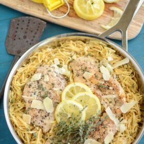Lemon Thyme Chicken served over pasta, topped with lemon, shaved parm, and rosemary in a skillet