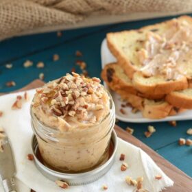 Pecan Honey Butter in a small mason jar topped with chopped pecans, sliced bread in the background
