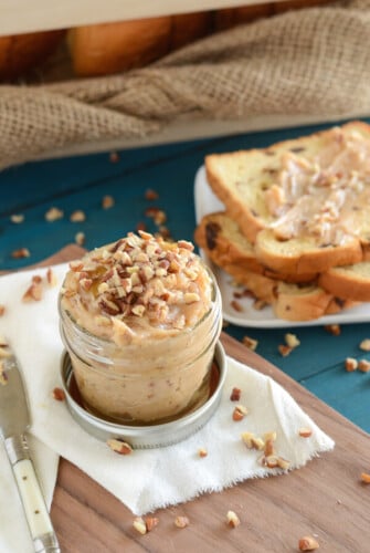 Pecan Honey Butter in a small mason jar topped with chopped pecans, sliced bread in the background