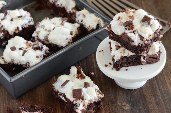 Rocky Road Brownies topped with marshmallows some in a back pan, others stacked on a white plate