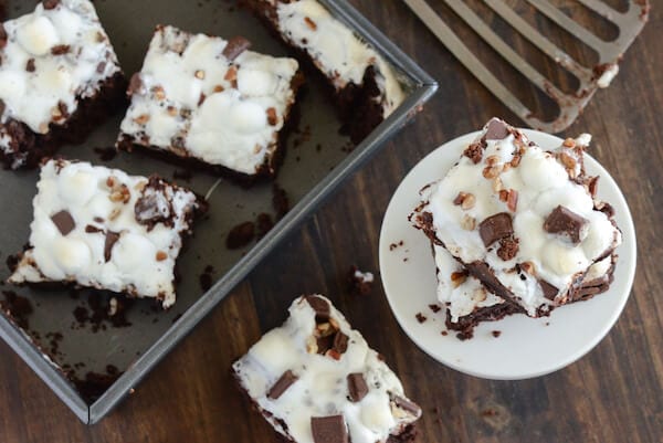 Rocky Road Brownies topped with marshmallows some in a back pan, others stacked on a white plate
