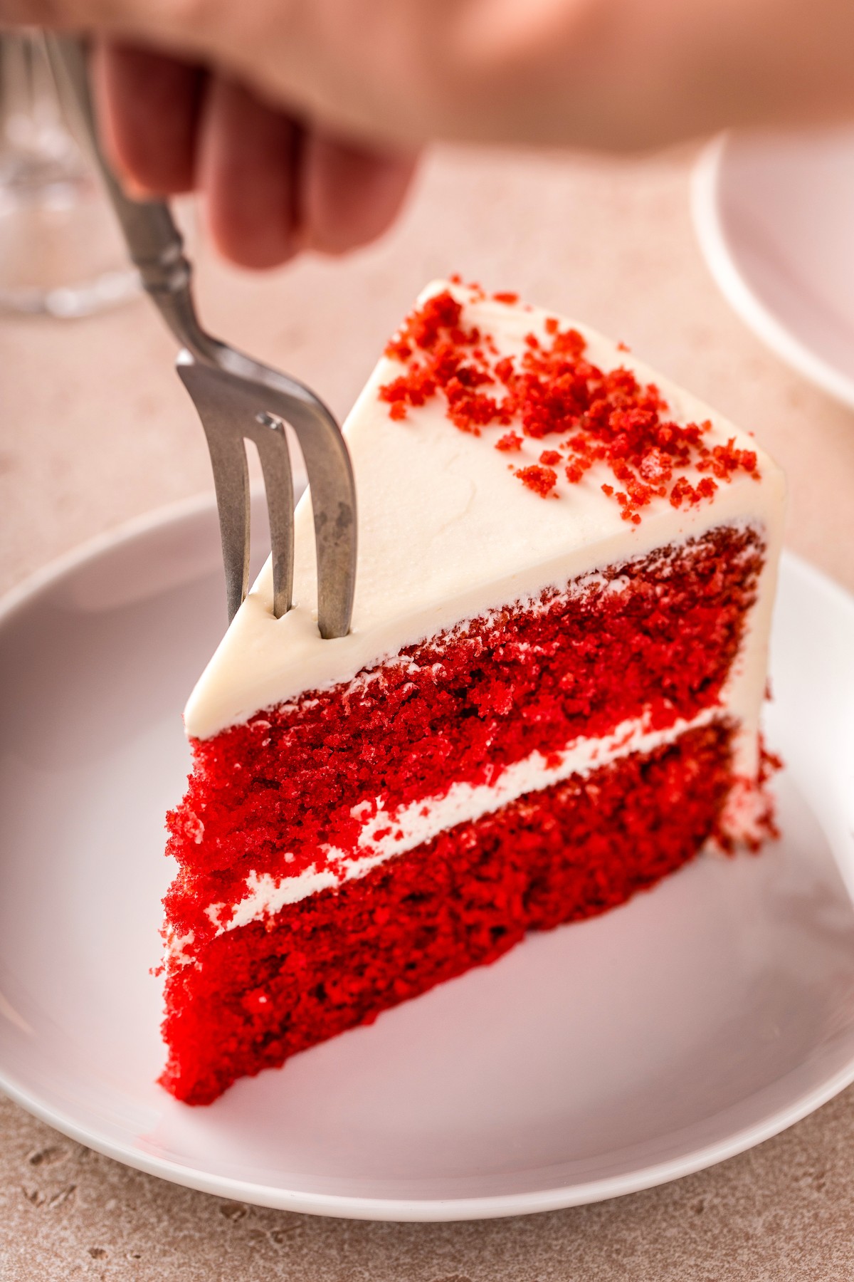 A fork piercing into a slice of frosted layer cake.