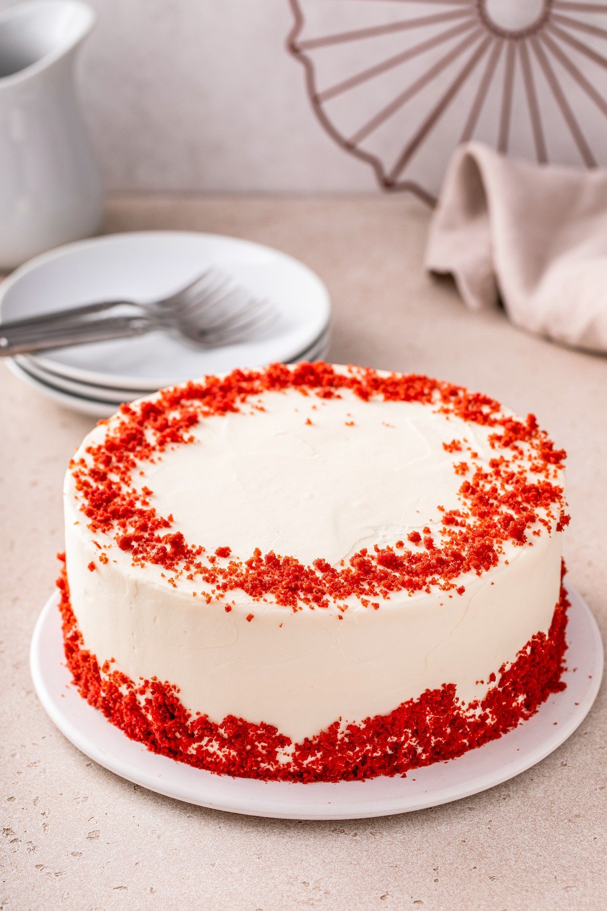 A red velvet cake frosted with cream cheese frosting, decorated with cake crumbs.