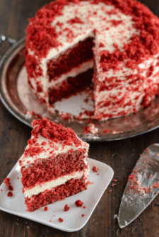 Slice of Red Velvet Dream Cake topped with Red Velvet cake crumbles served on a white plate