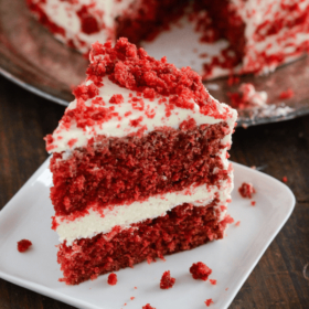Slice of Red Velvet Cake topped with cream cheese icing served on a white plate.