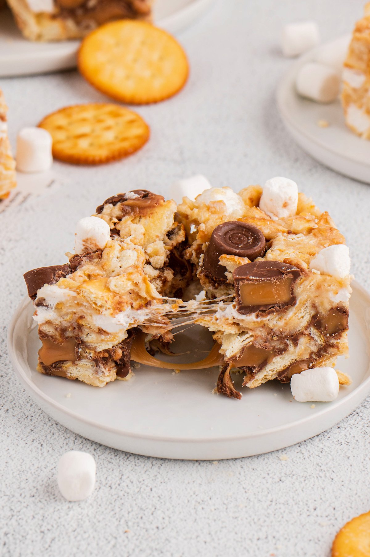 A rolo ritz marshmallow treat on a plate, pulled apart to show the gooey texture of the candies and marshmallow.