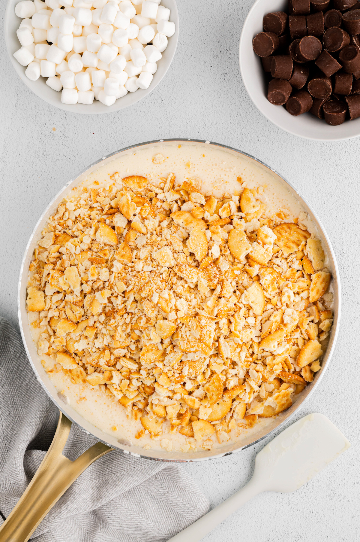 Crushed Ritz crackers dumped on top of a mixing bowl of melted marshmallow mixture.