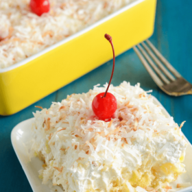 Twinkie, Pineapple & Coconut No Bake Cake on a white plate topped with shredded coconut and a cherry