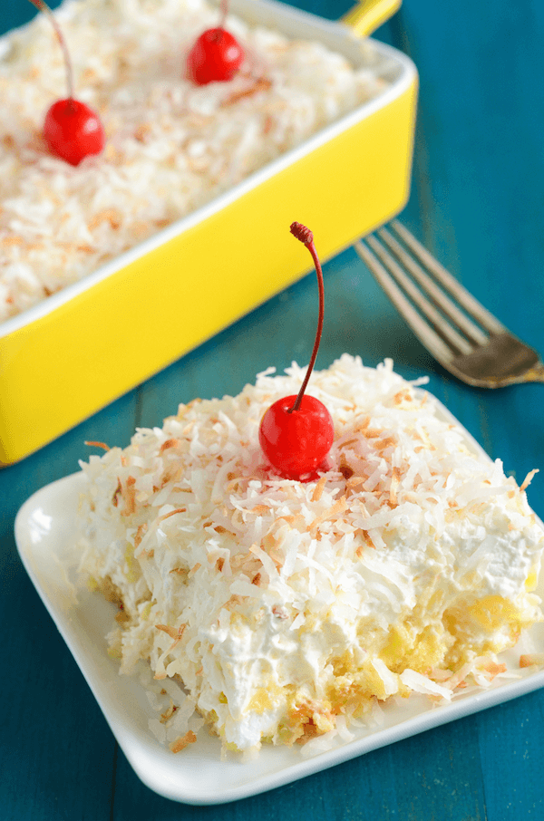 A serving of Twinkie Pineapple Coconut Cake on a white plate topped with shredded coconut and a cherry