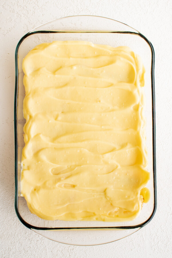 Vanilla pudding spread over layers of dessert ingredients in a glass dish.