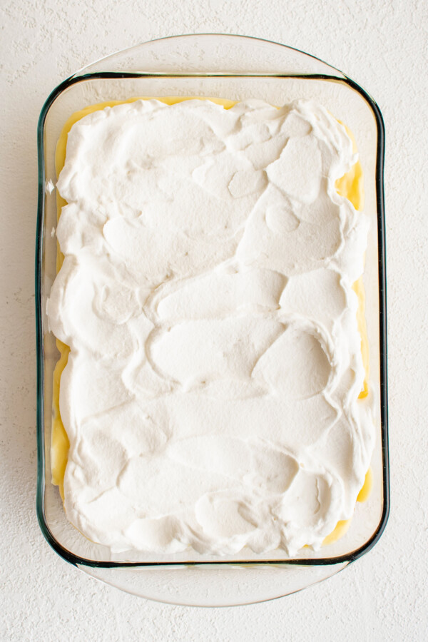 Whipped cream spread on top of other dessert ingredients in a glass baking dish.