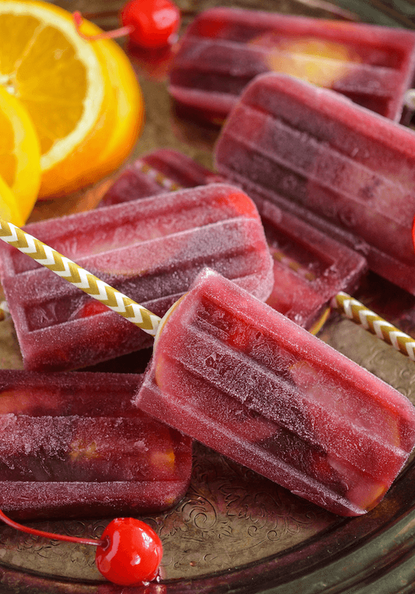 Sangria Popsicles with oranges and cherries on white and gold popsicle sticks on a serving tray