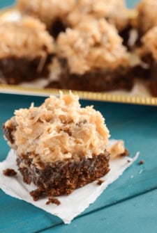 A German Chocolate Brownie on a Piece of Paper Towel with a Platter Holding More Browies in the Background