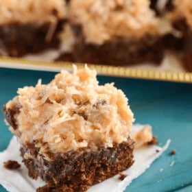 A German Chocolate Brownie on a Piece of Paper Towel with a Platter Holding More Browies in the Background