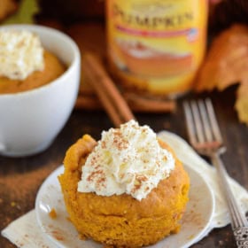 Pumpkin Mug cake set on a white plate topped with whipped cream and cinnamon