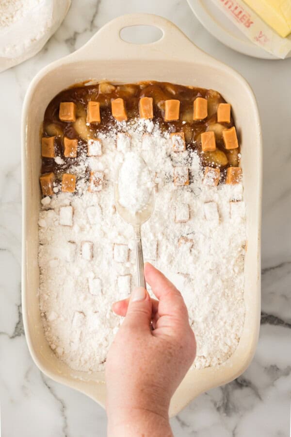 Cake mix sprinkled on top of caramel apple filling in a casserole dish.