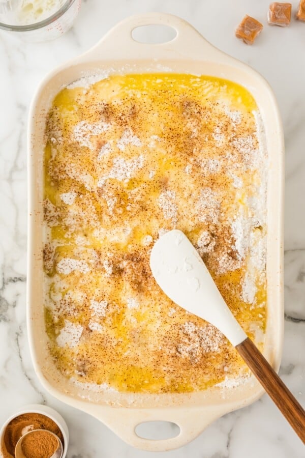 Melted butter spread across the top of assembled dump cake in a baking dish.