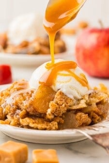 Caramel sauce is drizzled on top of a serving of caramel apple dump cake with a scoop of vanilla ice cream.