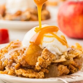 Caramel sauce is drizzled on top of a serving of caramel apple dump cake with a scoop of vanilla ice cream.