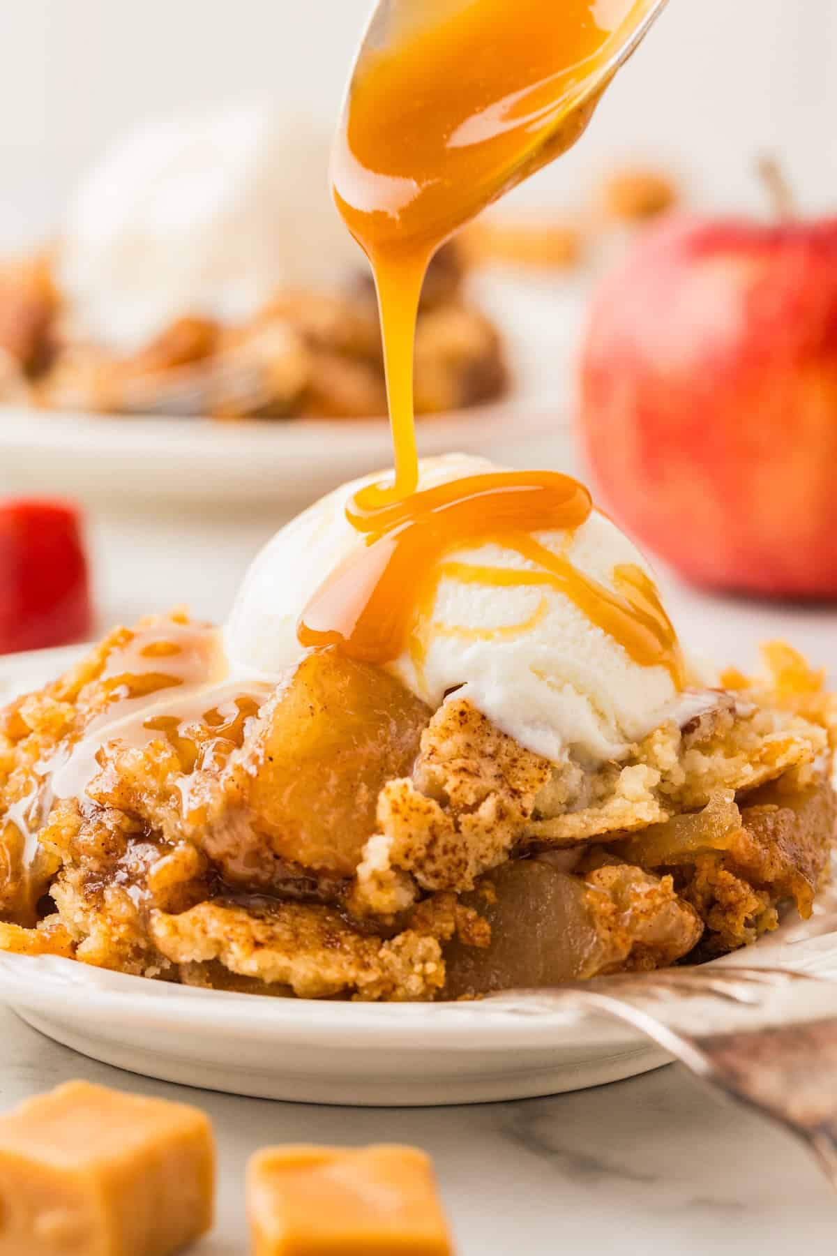 Caramel sauce is drizzled on top of a serving of caramel apple dump cake with a scoop of vanilla ice cream.