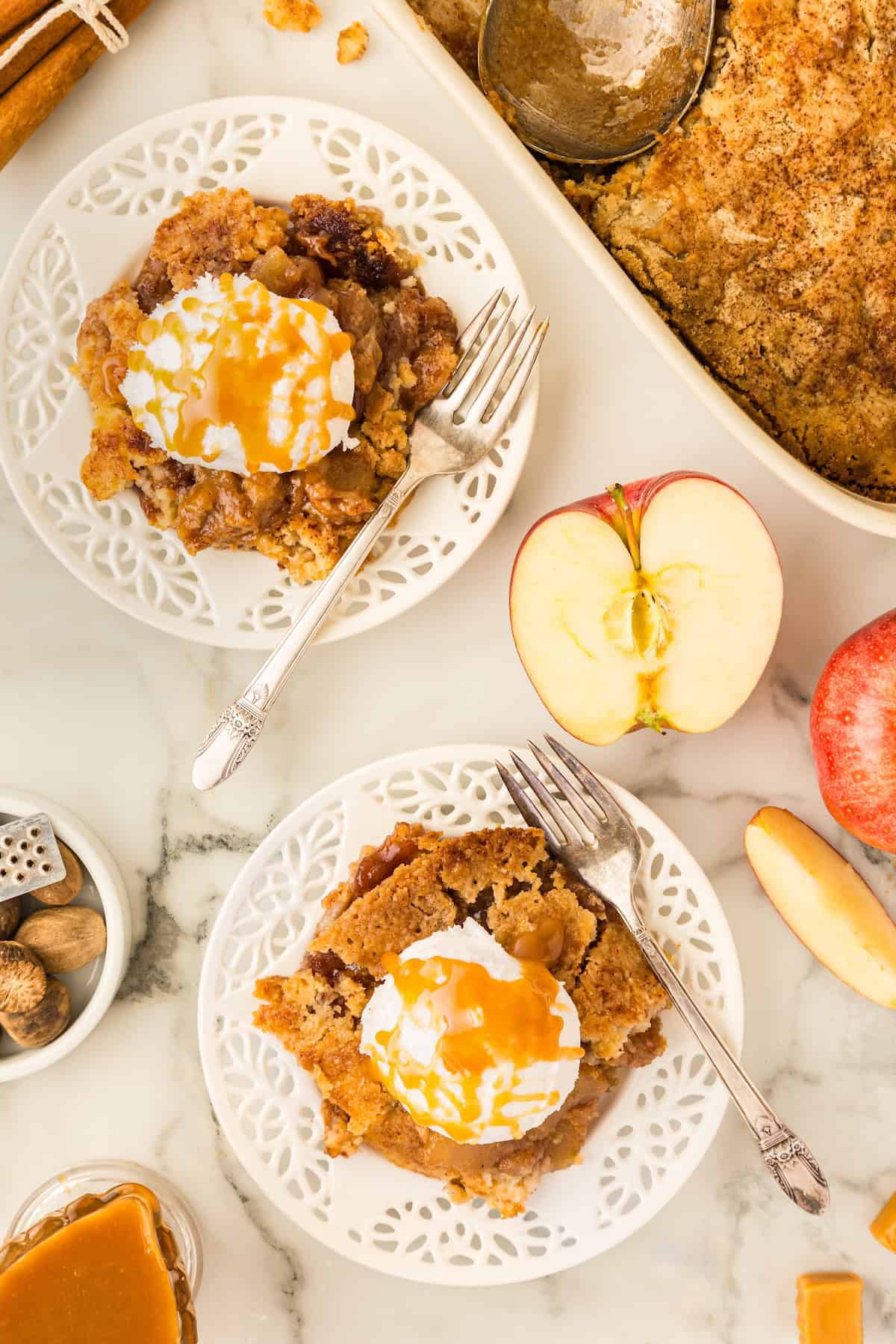 Servings of apple cake with ice cream and caramel sauce placed next to halved apples.