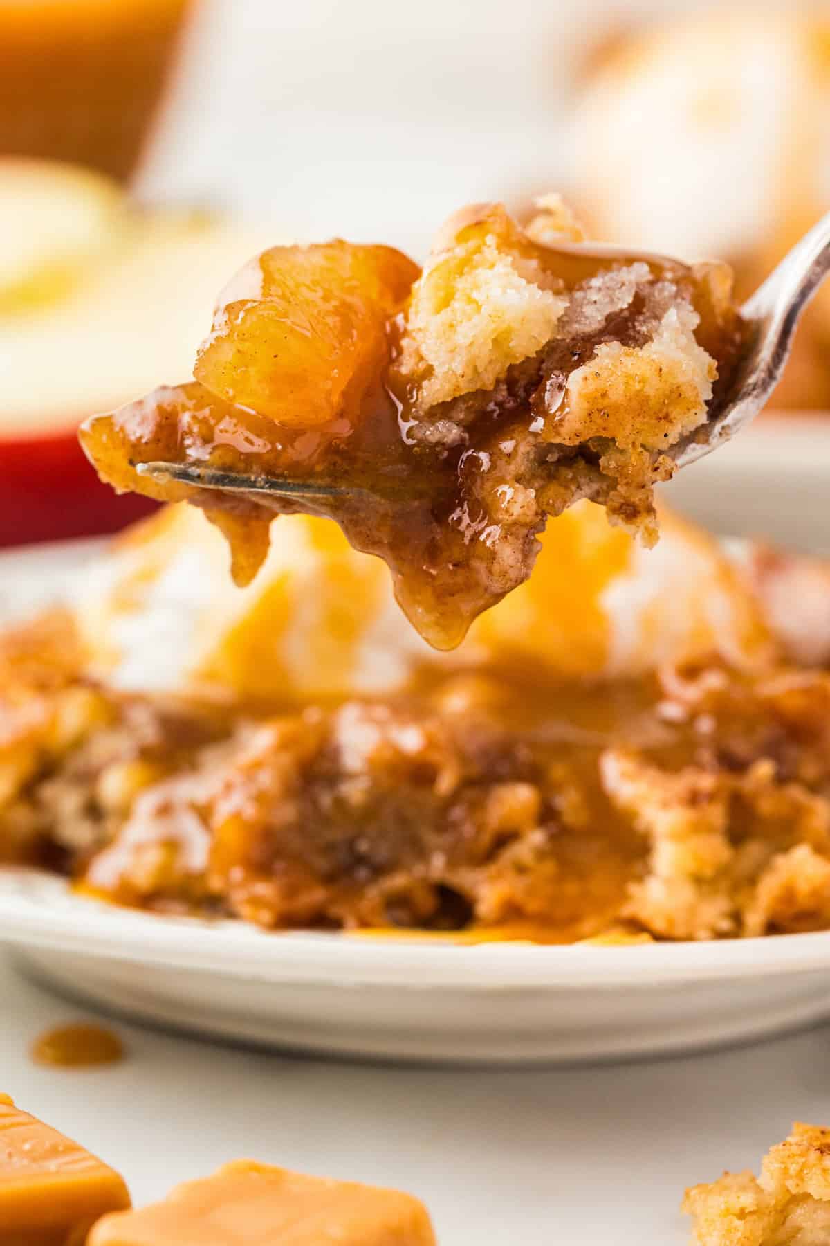 A forkful of caramel apple dump cake is lifted from a plate.