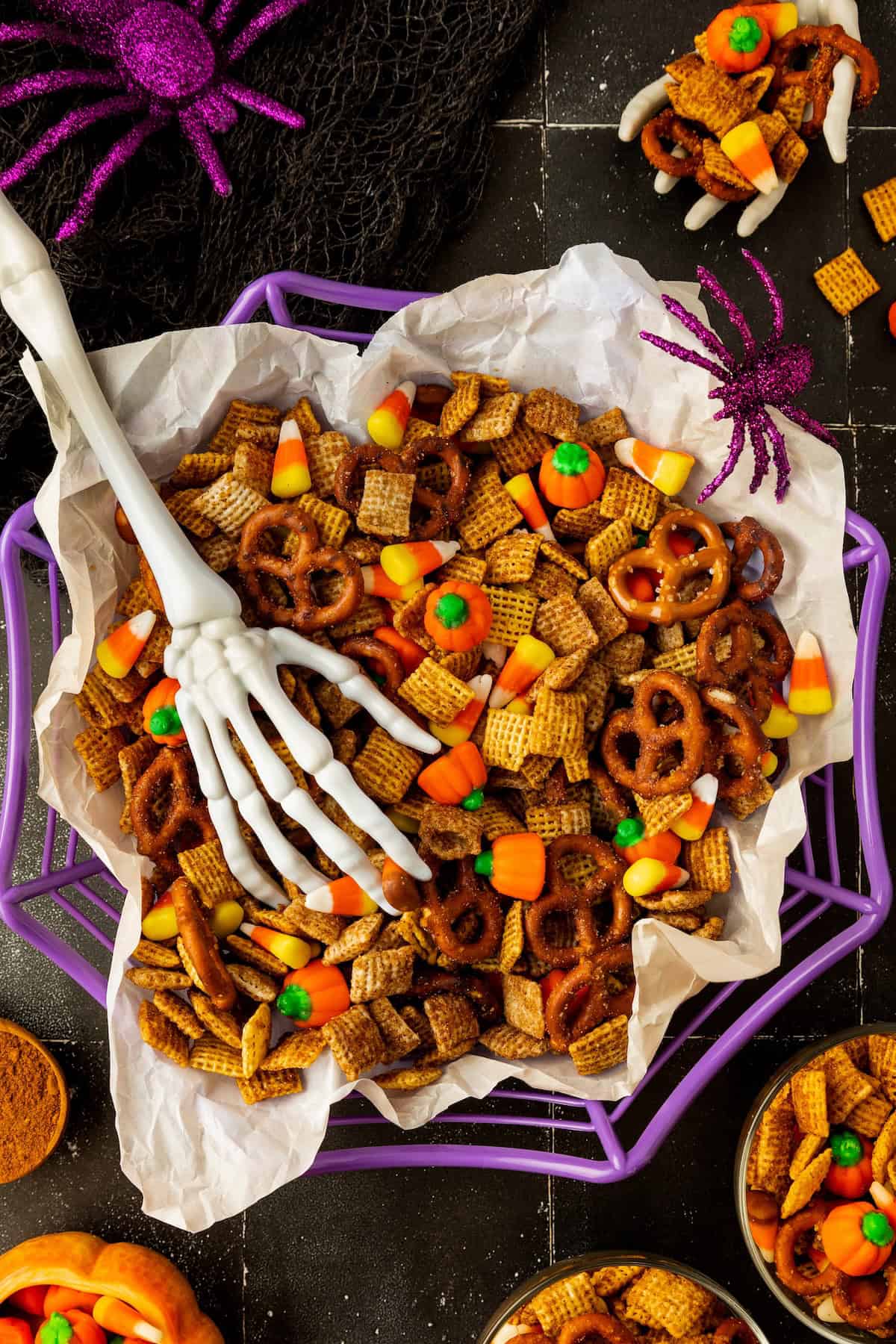 A decorative skeleton hand placed on a bowl of pumpkin spice chex mix.