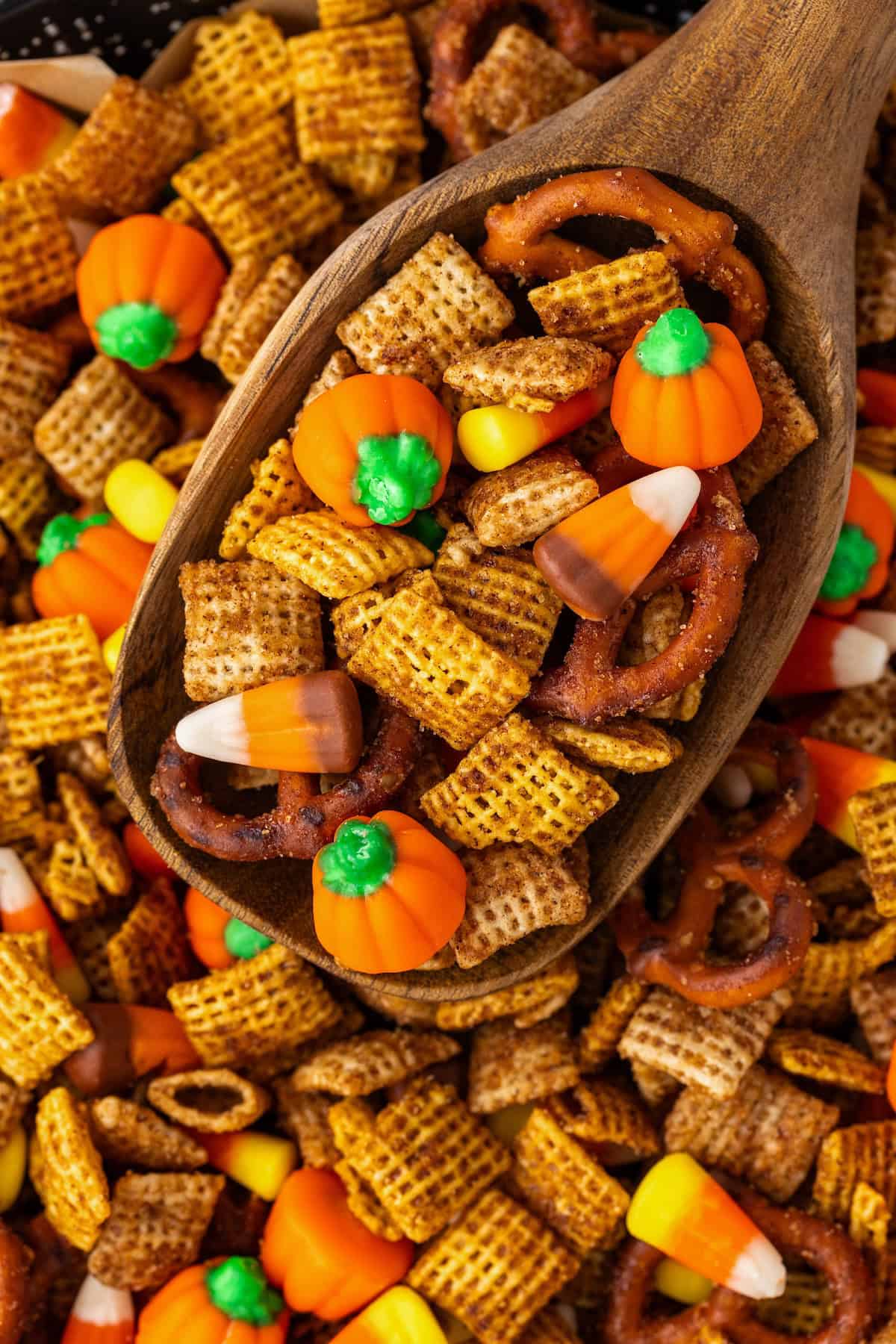 A large wooden serving spoon scooping Halloween chex mix.